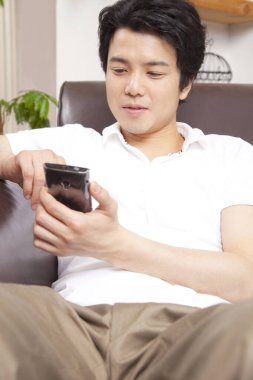 Asyalı adam kanepede otururken akıllı telefon kullanıyor. 