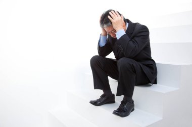 Kafası elinde merdivenlerde oturan takım elbiseli üzgün bir işadamı.