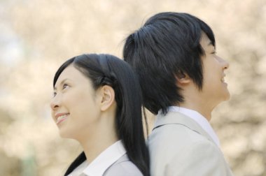 Parkta çiçek açan ağaçlara karşı poz veren Asyalı iş çifti