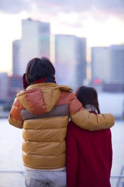 Kış kıyafetleri içinde genç bir çift şehre, arka plana, bulanık arka plana bakıyor. 