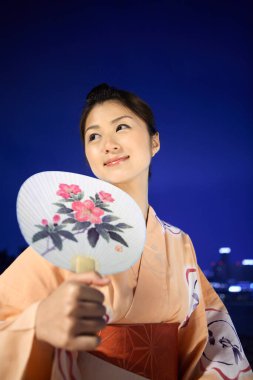 Geleneksel kıyafet giymiş genç Japon kadın elinde yelpaze, mavi arka plan 