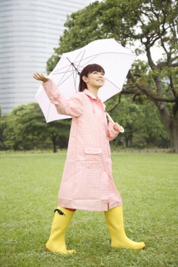 Yağmurluklu kadın şemsiye tutuyor. 