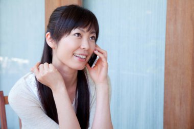 Kadın pencere kenarında cep telefonuyla konuşuyor. 