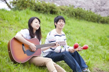 Genç Asyalı çift gitar ve marakas çalıyor.