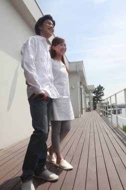 Ahşap bir güvertede bir binanın yanında duran bir çift.