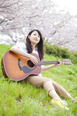 Parkta gitar çalan Asyalı kadın.