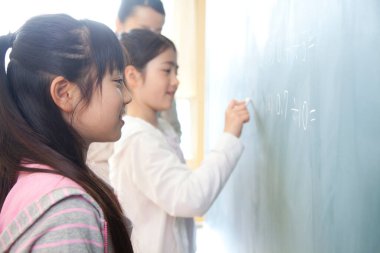 Japon liseli kızlar ve öğretmen okulda karatahta üzerinde alıştırma yapıyorlar.