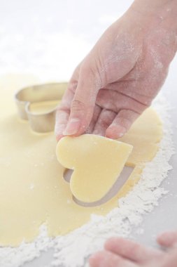 Kurabiye kesiciyle kalp şeklinde hamur işi yapan kişi 