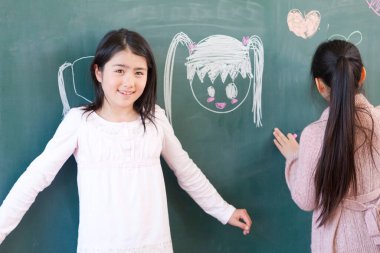 Asyalı kızlar tahtaya tebeşirle resim çiziyorlar. 