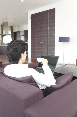 Kanepede dizüstü bilgisayarlı bir adam oturuyor.