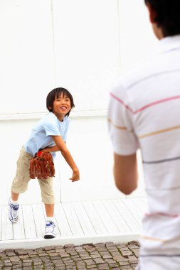 Gülümseyen çocuk dışarıda yetişkinlere beyzbol topu atıyor.