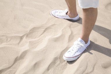 Sahilde duran beyaz spor ayakkabılı erkek bacaklarının kesilmiş fotoğrafı.