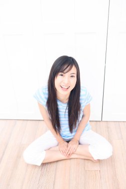 Yerde oturan Asyalı genç kız gülümsüyor. 