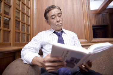 Olgun iş adamı odada kitap okuyor.