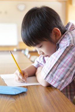 Küçük çocuk okulda kağıda yazıyor.