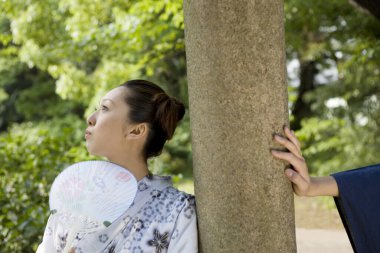Dışarıda, ağacın yanında yelpaze tutan kadın.