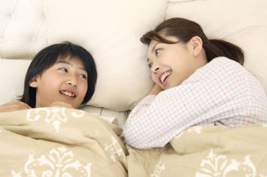 Genç Asyalı anne ve kızı yatakta birlikteler.