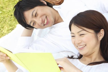 Genç Asyalı çift parkta kitap okuyor. 