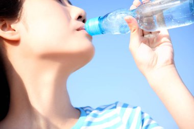 Mavi gökyüzüne karşı şişeden su içen kadın 