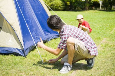 Asyalı baba ve oğlu kamp alanında çadır kuruyor.