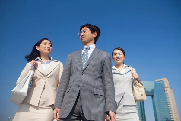 Portrait of handsome Japanese businessman with two business women posing outdoor on the street
