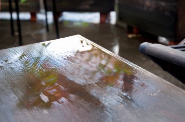 Islak ahşap masa dışarıdaki yeşilliği yansıtıyor.