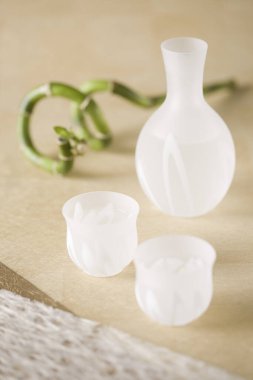 Buzlu cam vazo ve zarif bir şekilde dizilmiş iki küçük kupa.