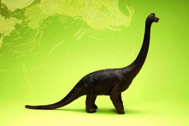 Şirin dinozor oyuncağı ve yeşil arka planda dünya haritası                     