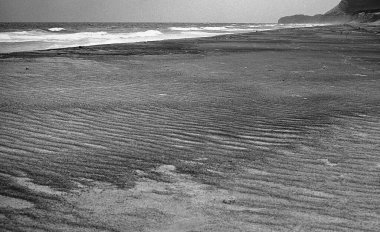 Dalgalı deniz ile kumlu sahil üzerindeki bulutlar, siyah ve beyaz çekim 