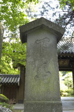 Açık havada yemyeşil ağaçların arasında duran yıpranmış taş sütun.