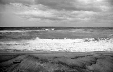 Dalgalı deniz ile kumlu sahil üzerindeki bulutlar, siyah ve beyaz çekim 