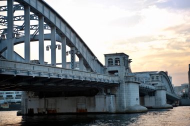 Gün batımında geniş nehir boyunca uzanan kemerli çelik köprü.