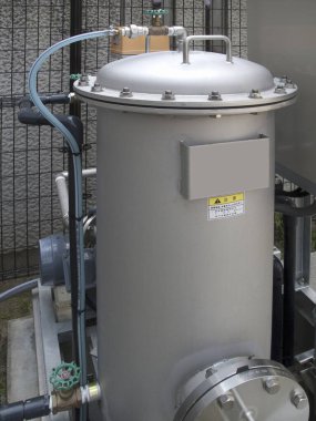 Boruların yanında duran büyük endüstriyel metal filtre kaplaması.