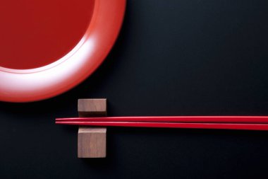 Kırmızı tabak ve ahşap çubuklar, Japon kültüründen esinlenerek, yukarıdan bakıldığında siyah bir zemin üzerine dizilmiş..