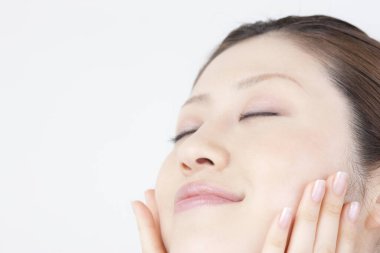 Güzel Japon kadın kendi yüz masajını yapıyor, beyaz arka planda yakın plan portresi. 