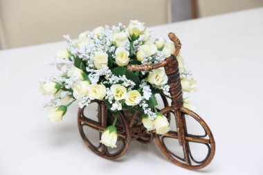 Masanın üzerinde küçük beyaz çiçekli ahşap bir bisiklet.