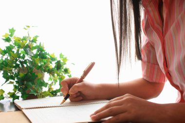 Genç bir kadın arka planda boş bir deftere yazı yazıyor. Kapat.