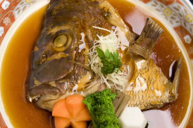 Közlenmiş balık kafası renkli sebzelerle servis edilir.