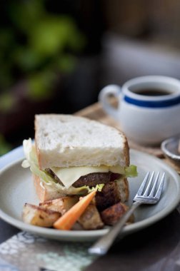 Sandviç ve fırında patates ve havuç ile masada bir fincan çay.