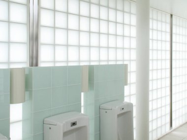 Beyaz pisuarların ve cam blokların bulunduğu modern tuvalet.