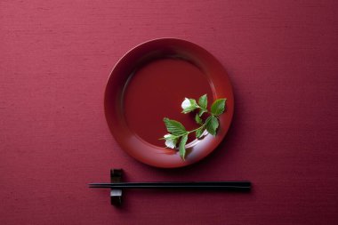 Canlı kırmızı bir zemin üzerinde ahşap yemek çubukları olan düz bir tabak Japon kültürünü yansıtıyor..
