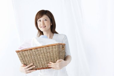 Beyaz gömlekli Asyalı kadın çamaşır sepetini tutuyor. 