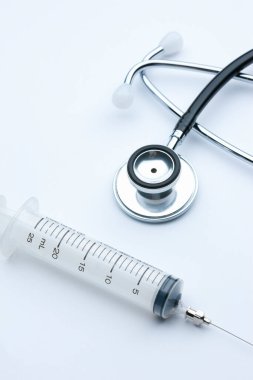 Beyaz arka planda tıbbi steteskop ve şırınganın yakın plan görüntüsü   