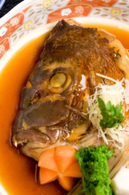 Buğulanmış balık kafası sebze ve otlarla süslenmiş.