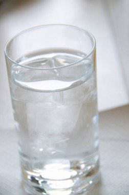 Beyaz masada buz küpleri olan bir bardak su.