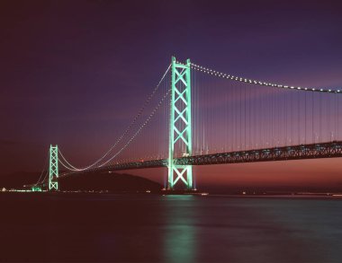 Alacakaranlıkta yansımalarla suya yayılan aydınlatılmış köprü