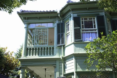 Güneşli yeşil Viktorya evinin dış tarafında süslü pencereler ve panjurlar var.