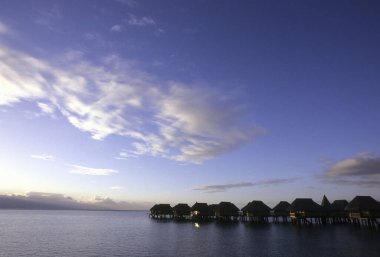 Su üzerinde bungalovları olan güzel bir gün batımı