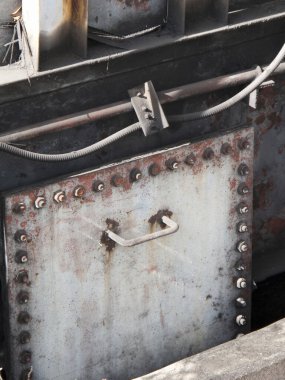 Paslı metal kapı, cıvatalar ve sanayi boruları var.