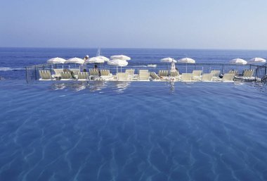 Açık mavi suyu olan yüzme havuzu, yaz mevsiminde şemsiyeli beyaz sandalyeler ve deniz manzarası